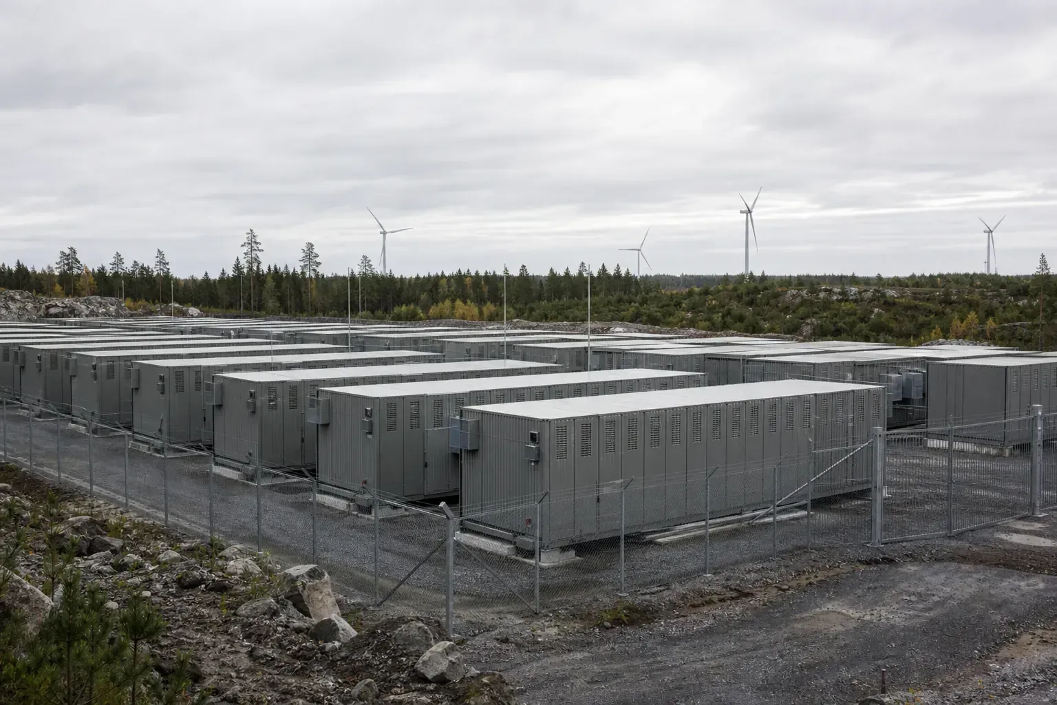 Storskaligt batterilager med rader av containrar intill en vindpark