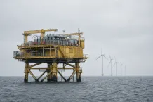 Gul havsbaserad transformatorstation till havs med vindkraftverk i bakgrunden