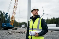 Projektledare med ritningar på en vindkraftsbyggarbetsplats med kran och torndelar