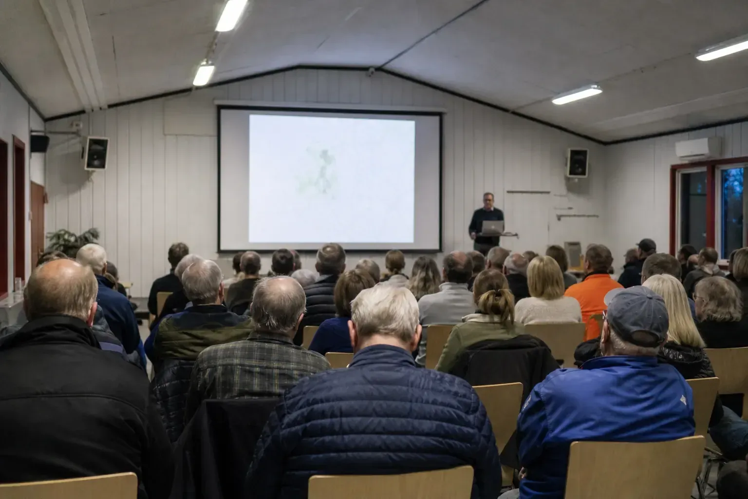 Samrådsmöte i en bygdegård med åhörare framför en projektorduk
